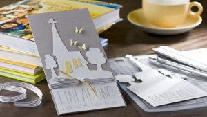 Ideen für Kommunion und Konfirmation: Komm zur Kirche | Einladung in Taupe und Weiß mit der Silhouette einer Kirche, zartgelben Schmetterlingen und einem geradlinigen Schriftzug
