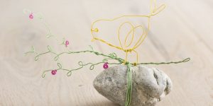 Ideen für Papierdraht: Blütenglück | Gelber Vogel, grüner Zweig und Blüten in Pink aus Papierdraht auf einem Kieselstein