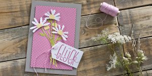 Ideen für Glückwünsche und Grußkarten: Blumen sagen mehr als 1000 Worte | Graue Glückwunschkarte mit einem kleinen, weiß-gelben Blumenstrauß aus Papier vor einem Karo-Hintergrund in Pink
