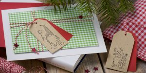 Ideen für die Weihnachtspost: Es wichtelt in der Weihnachtszeit | Lustige Weihnachtskarte in Rot, Grün, Weiß und Natur mit einem stilisierten Geschenk und einem Anhänger mit handgezeichneten Wichteln