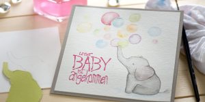 Ideen für Babys: Das große Glück ist manchmal ganz klein | quadratische Karte für Geburtsanzeigen mit einem aquarelliertem Elefanten, der über dem gestempelten Schriftzug (Unser Baby ist angekommen) Seifenblasen in Regenbogenfarben aus dem Rüssel pustet.