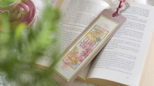 Ideen für Glückwünsche und Grußkarten: Farbenfrohe Wünsche für Buchliebhaber | ein Lesezeichen mit aquarelliertem Hintergrund und einem gestempelten Motiv, das aus mehreren Blütenköpfen besteht, die an Margeriten oder Astern erinnern, und einem handgeschriebenen Text: Glückswunsch.