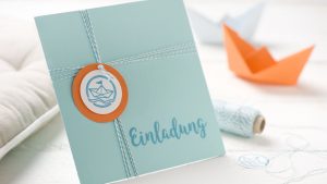 Ideen für Kommunion und Konfirmation: Auf den Punkt gebracht | Quadratische Einladungskarte in Azur und Orange mit einem gestempelten Text im Handlettering-Stil (Einladung) und einem gestempelten runden Motiv: Ein kleines Origami-Schiff